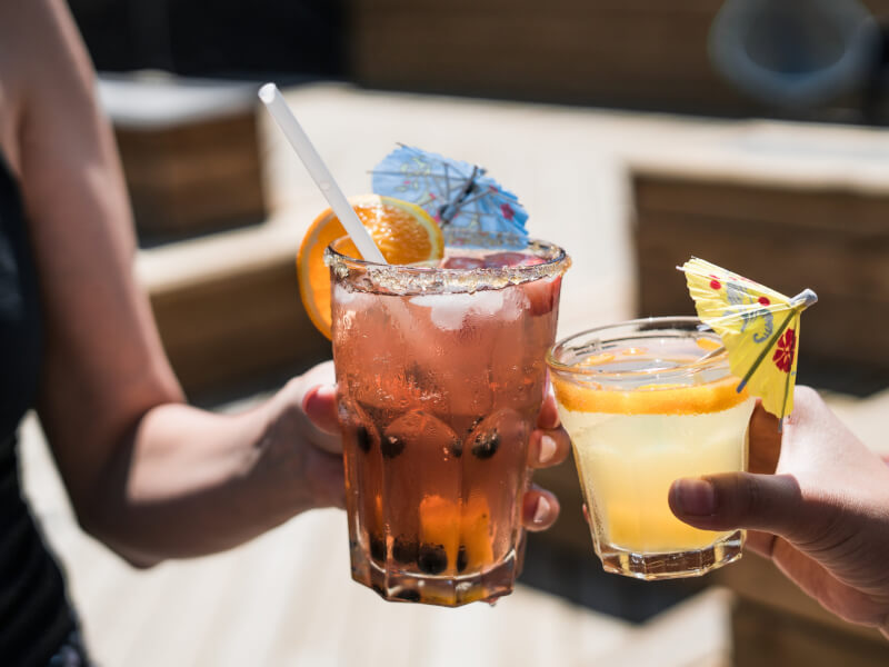 2 people holding cocktails clink glasses